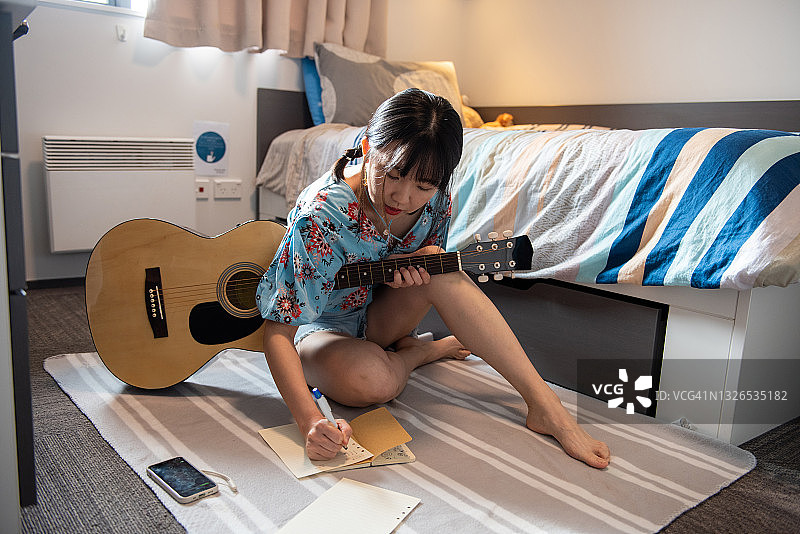 一位年轻的亚洲女音乐家正在用她的手机应用和吉他谱曲图片素材