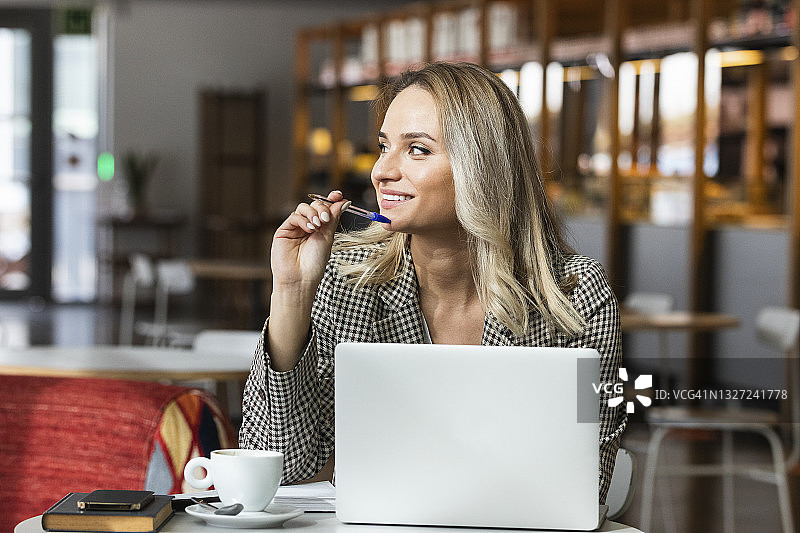 微笑的职业女性看着别处，而坐在咖啡馆笔记本电脑图片素材