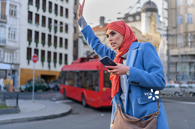 一位年轻的穆斯林妇女站在城市的街道上，试图赶上一辆出租车。图片素材