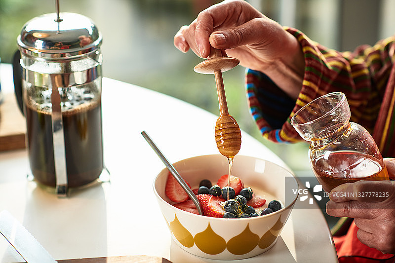 女人用蜂蜜勺把蜂蜜倒在一碗新鲜水果上图片素材