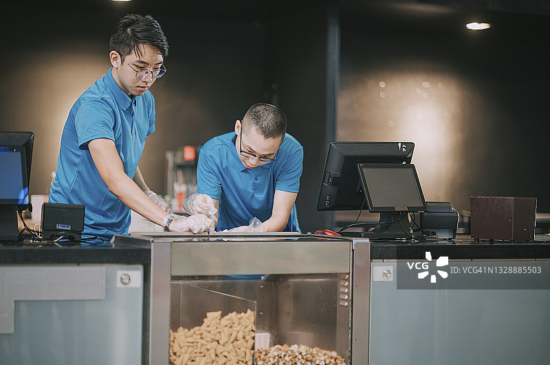 电影放映时间开始前，亚洲华人男子在电影院吧台准备爆米花图片素材