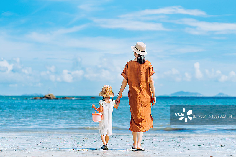 后视图深情年轻的亚洲母亲和小女儿手牵手散步，分享时刻在海滩上漫步在一个阳光明媚的夏天图片素材