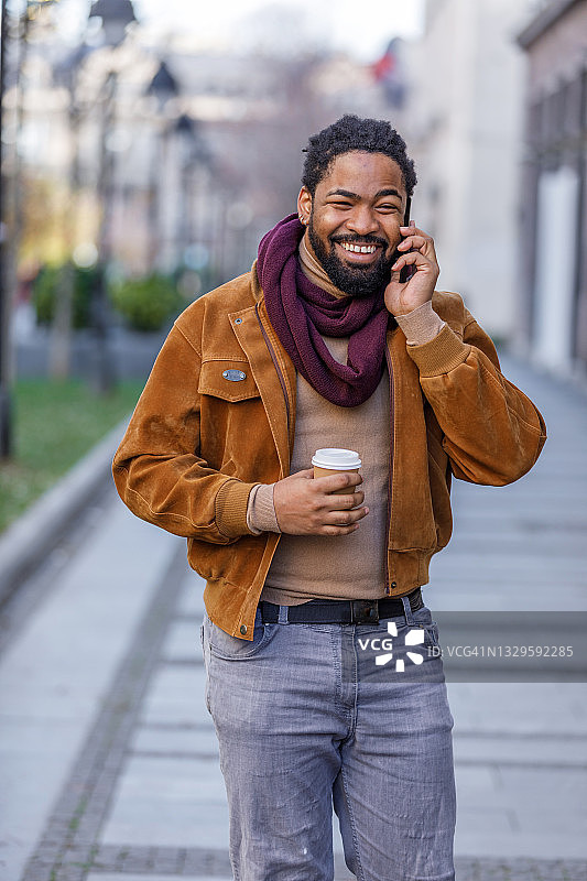 一个英俊的非洲人用手机走在城市的街道上，喝着咖啡，用着电话。图片素材