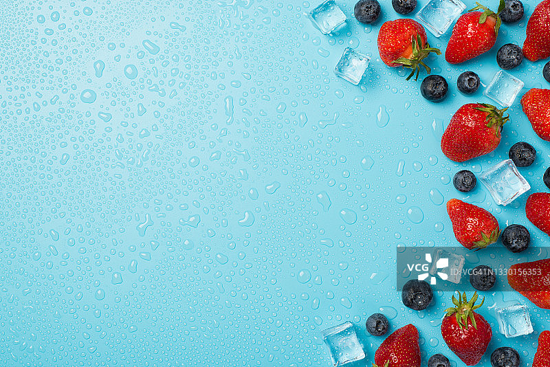 头顶上的照片，一堆蓝莓、草莓、冰块和水孤立在蓝色背景与空的空间图片素材