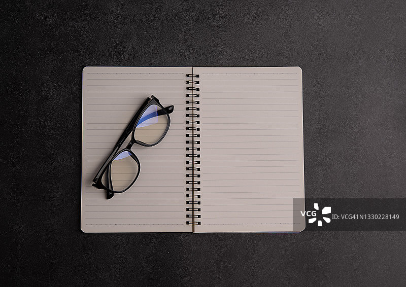 眼镜放在打开的笔记本上，笔放在黑色的桌子上图片素材