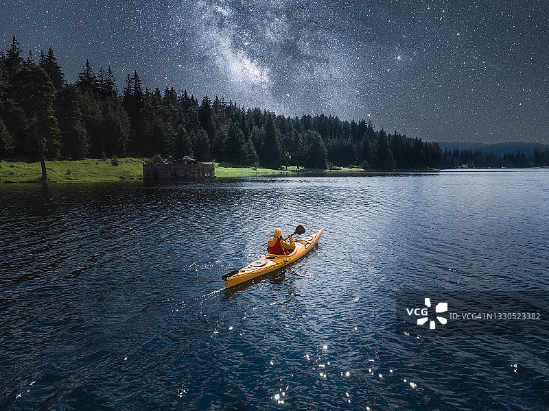 一个女人在银河下的高山湖泊里划独木舟。星空鸟瞰图。划和生态旅游。图片素材