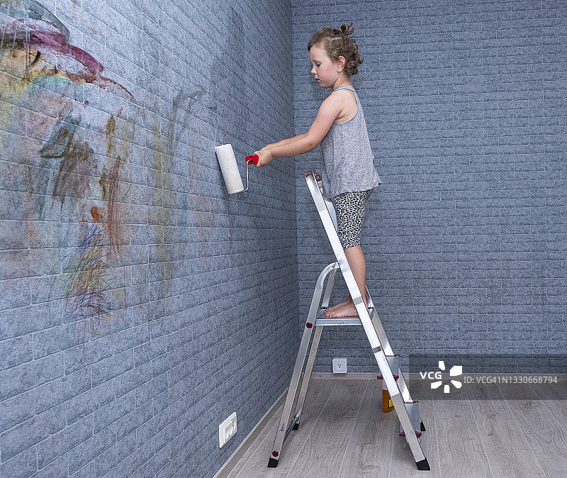 孩子，白人女孩手里拿着油漆滚筒。女孩刷墙。图片素材