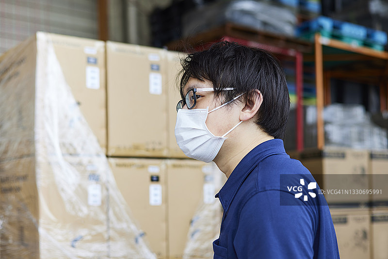一名在仓库工作的年轻人，在冠状病毒大流行期间戴着口罩图片素材