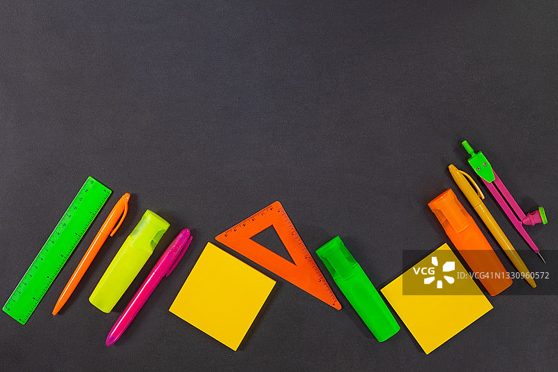回到学校。绿色、黄色、粉红色、橙色的办公用品都在黑板上、桌子上。前视图。尺子，记号笔，毡尖笔，圆规，钢笔，便签。本空间图片素材