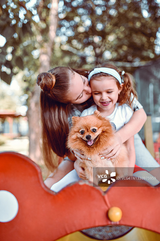 在操场上和可爱的博美犬玩耍的时候，女孩亲吻了孩子的妹妹图片素材