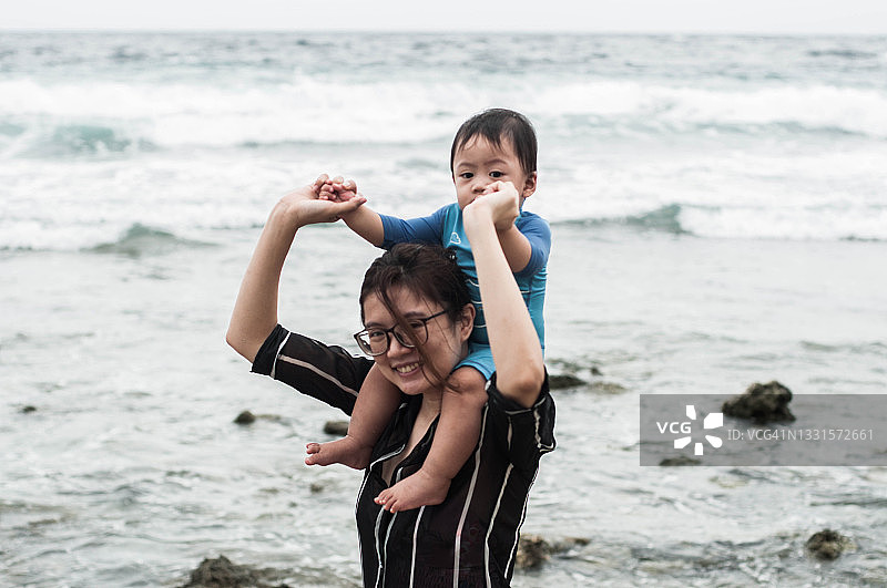 一位东南亚母亲背着儿子走在沙滩上图片素材