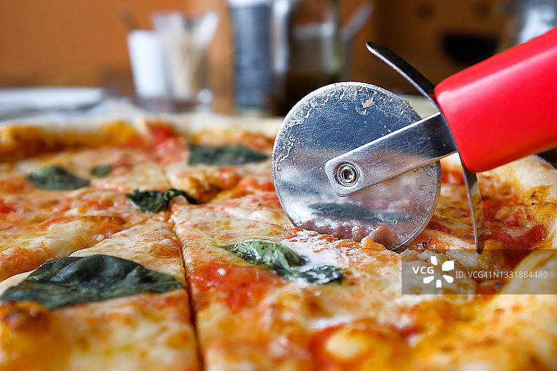 在披萨店、咖啡馆或快餐店的餐桌上，木架或切菜板上，有马苏里拉奶酪、罗勒叶和酱的玛格丽塔披萨。就在切披萨的刀旁边。传统的意大利美食。素食。特写镜头。图片素材