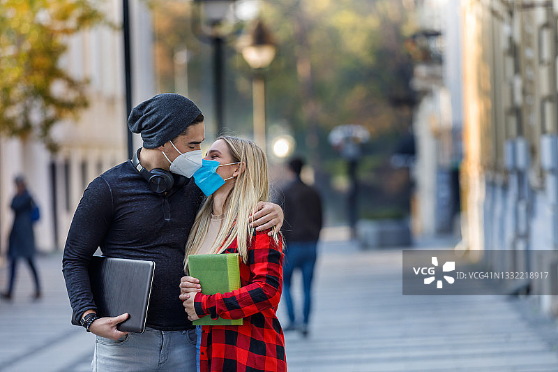 一对快乐的年轻情侣戴着面具在城市街道上拥抱亲吻，并进行着愉快的交谈。图片素材