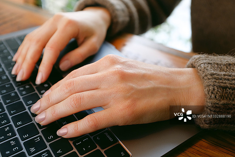 女性的手在电脑或笔记本电脑的键盘上打字，在咖啡馆或共同工作的空间。一位办公室职员在他的办公桌前。商业的概念，自由职业，在家工作。特写镜头。图片素材
