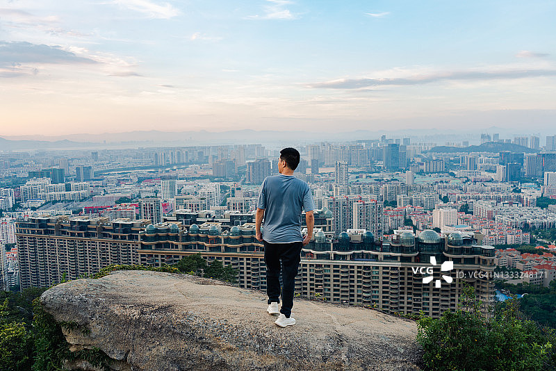 一个亚洲人站在一块岩石上鸟瞰城市的建筑图片素材