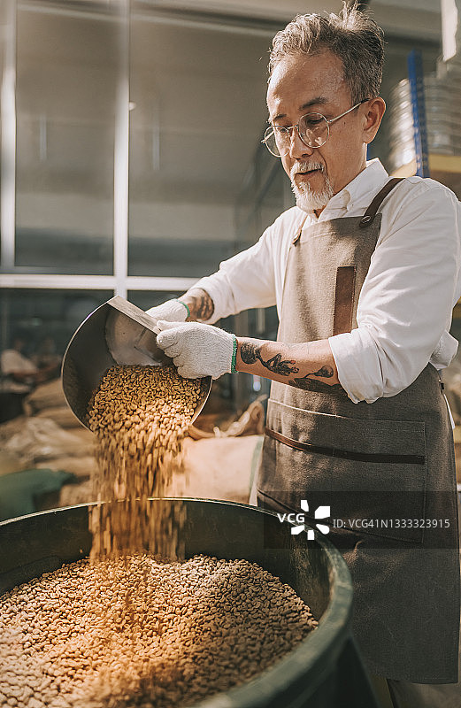 亚洲华人高级工作人员将生咖啡豆从桶中舀到秤机上，并将其混合在工厂仓库的咖啡烘焙过程中图片素材