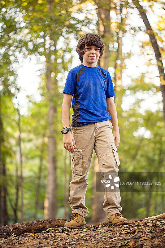 微笑的男孩站在树干在树林里，美国图片素材