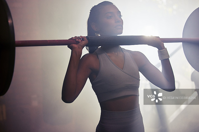一个运动的年轻女人准备在健身房做杠铃顶压图片素材