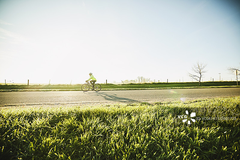 在春日早晨的日出，高级女自行车手在训练骑上的极端宽镜头图片素材