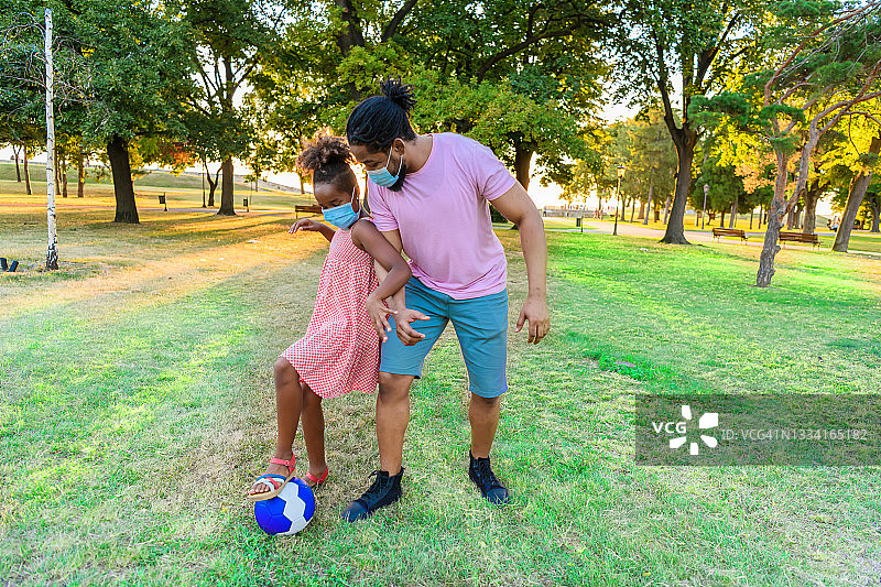 在冠状病毒时代，快乐的非洲裔父亲和女儿在户外玩足球。图片素材