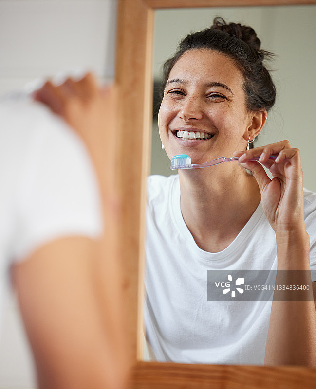 一名年轻女子一边刷牙一边对着浴室的镜子图片素材