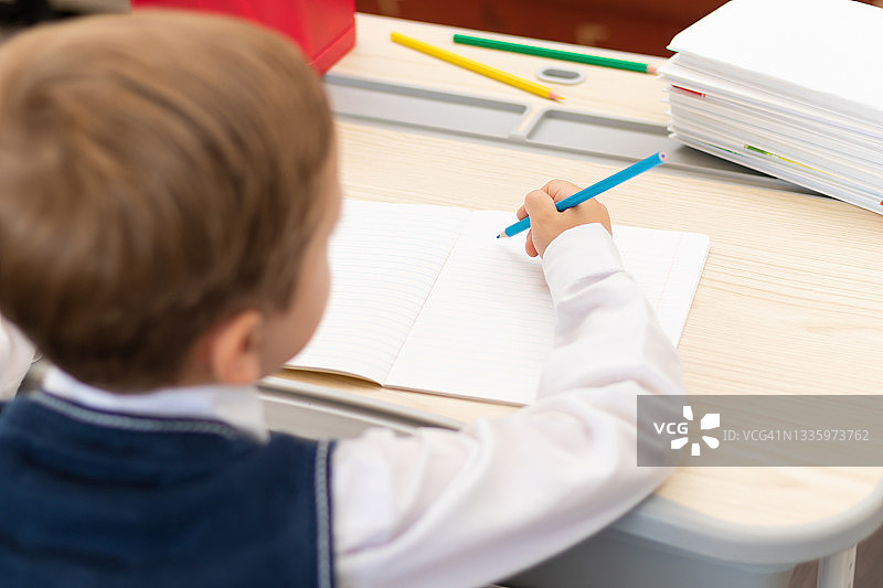 身穿校服的一年级男生在家里拿着铅笔坐在书桌前做作业。远程教育。有选择性的重点。特写镜头图片素材