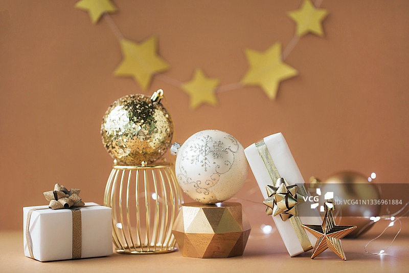 圣诞构图由两件白色礼物，金色的星星，金色的讲台上三个不同的球和米色背景上的花环组成。新年概念图片素材