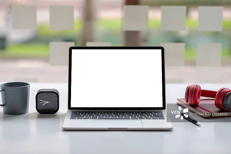 笔记本电脑空白的白色屏幕和耳机放在一个白色的桌子。模拟。图片素材