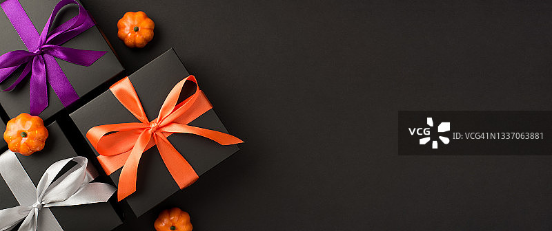 顶视图照片的三个黑色礼品盒紫罗兰橙和白色丝带蝴蝶结和小南瓜在孤立的黑色背景与copyspace图片素材