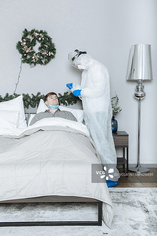 在新年和圣诞节前，一名穿着个人防护服、戴着手套和口罩的医生在患者家中用棉签检测冠状病毒covid-19图片素材
