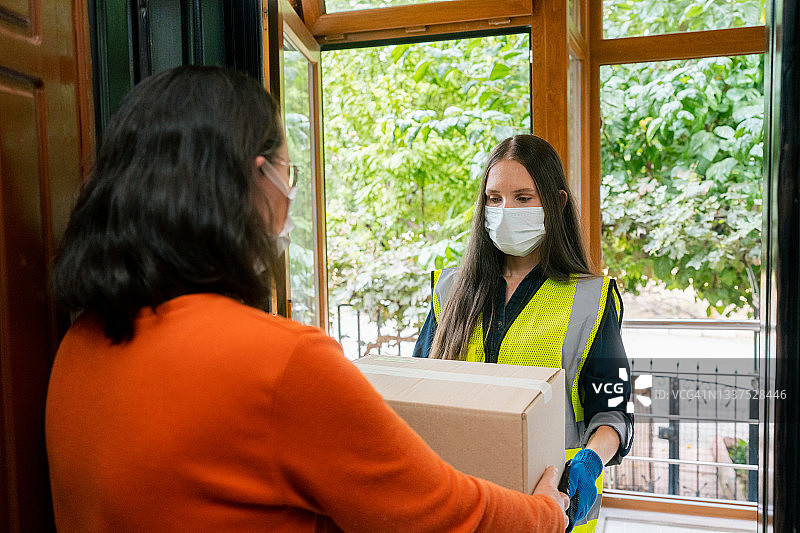 女快递员戴着防护口罩在家给顾客送包裹。客户收到她的包裹图片素材