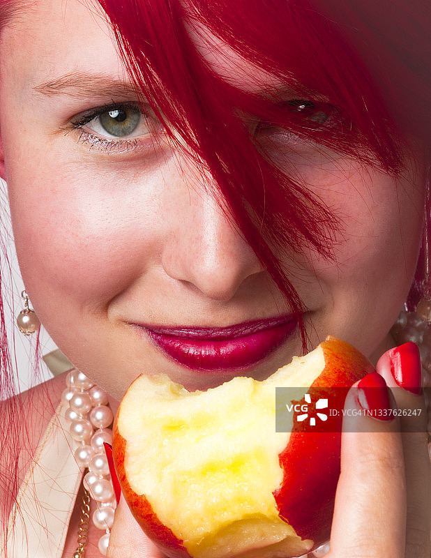 一个长着一头亮红色头发，手里拿着一个红苹果的女人的肖像图片素材