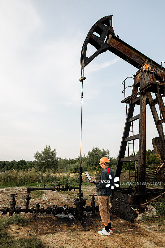 石油工人正在用笔记本电脑检查油田油井抽油机的工作情况图片素材