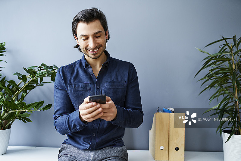微笑的职业男性在办公室的墙壁前使用智能手机图片素材