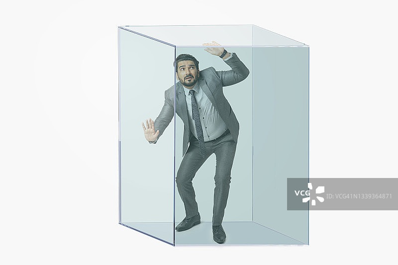 一个穿着正装的男人被困在一个透明的立方体里。图片素材