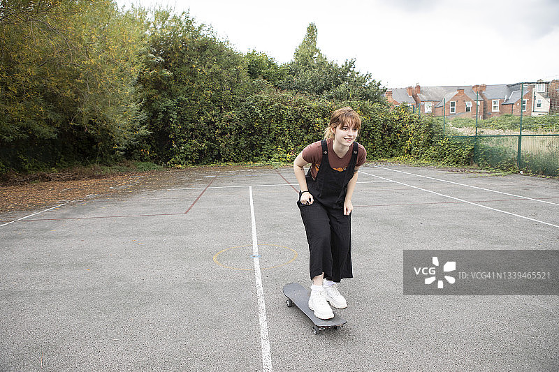 女学生在一个废弃的网球场玩滑板图片素材