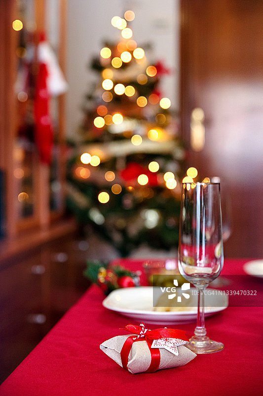 舒适的桌子上铺着红色的桌布，为一个人准备了一个小礼物细节，后面是圣诞树的灯图片素材