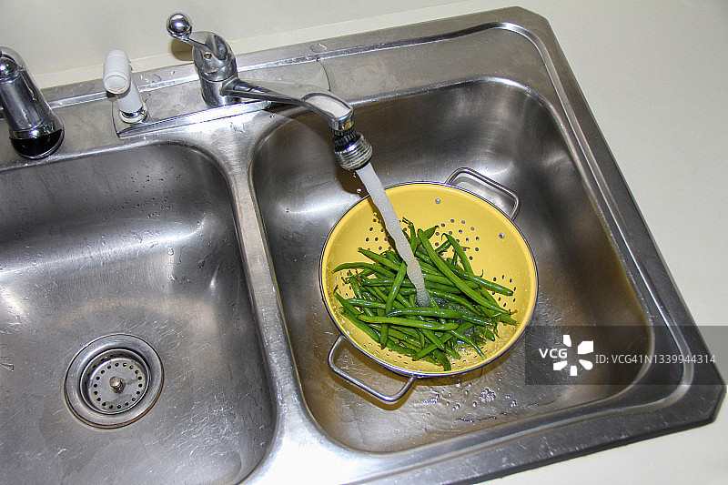 厨房水槽里的水在滤锅里的青豆上流淌图片素材