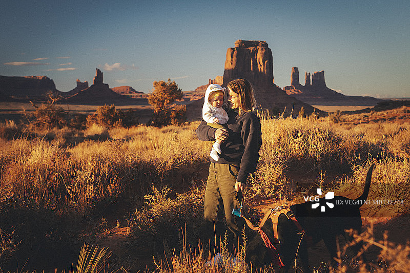 一名妇女抱着孩子和一只狗站在亚利桑那州纪念碑谷图片素材