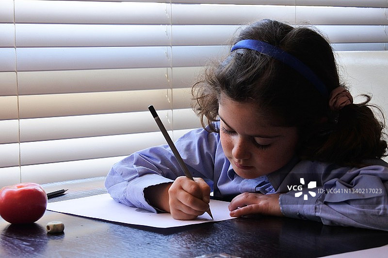 一个年轻的女孩用铅笔在白纸上画一个成熟的红西红柿图片素材