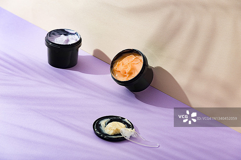 用于身体和面部皮肤护理的天然产品。橘色奶油，黑色罐子，紫色和米色背景图片素材