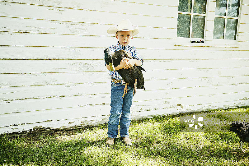 一个夏天的早晨，一个小男孩在鸡舍外抱着一只鸭子图片素材