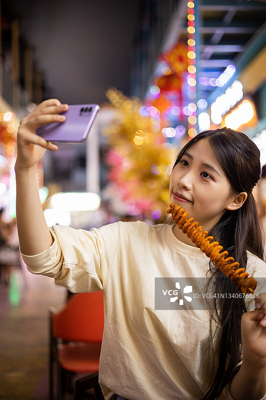 年轻女子在夜市街上用手机自拍图片素材