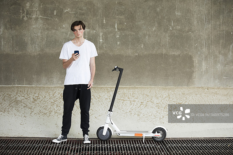一个十几岁的男孩站在地下室的电动滑板车旁边听音乐图片素材