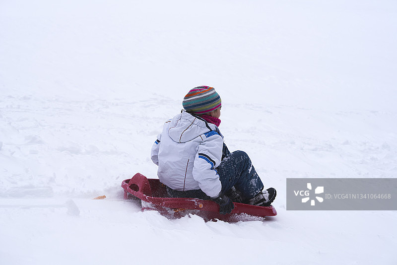 后视图的女孩与雪橇滑在积雪覆盖的领域图片素材