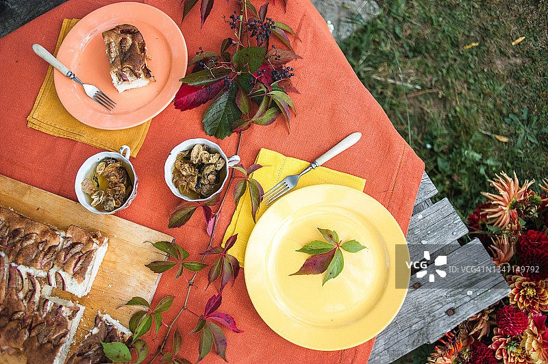 明亮的秋天静物，橙色和黄色的南瓜，鲜花，杯草药茶和夏洛特苹果派在木制砧板像托盘一样放在桌子上，覆盖着室外的橙色亚麻桌布。图片素材