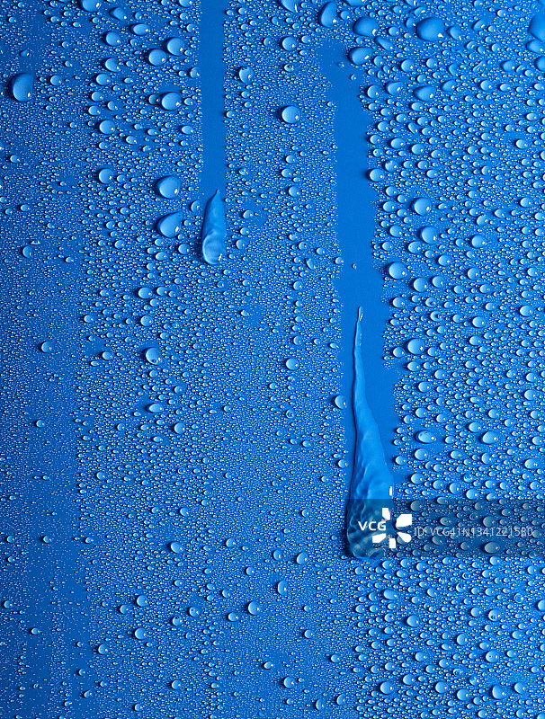 水滴在蓝色潮湿的表面上滑动的完整框架。图片素材