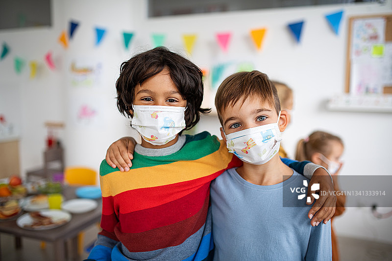 两名同学戴着口罩站在教室里，抱着肩膀，冠状病毒概念。图片素材