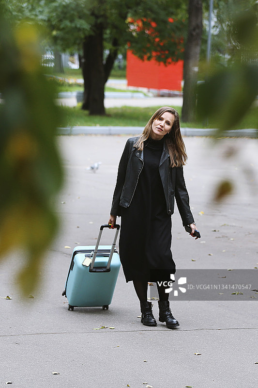年轻美丽的女人穿着黑色皮夹克推着行李图片素材