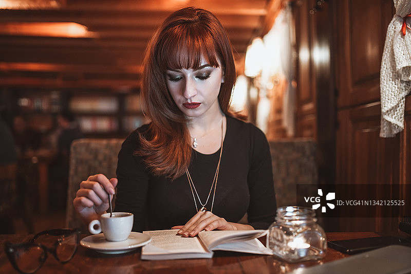 美丽的红发在酒吧边喝咖啡边看书图片素材